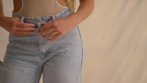 Close-Up-Studio-Shot-Of-Woman-Putting-Fingers-Through-Belt-Loops-Of-Denim-Jeans